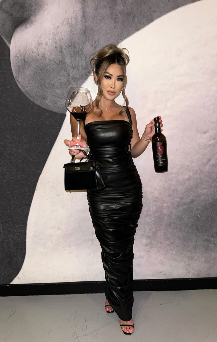 Woman in a black dress holding a glass and bottle against a stylized background