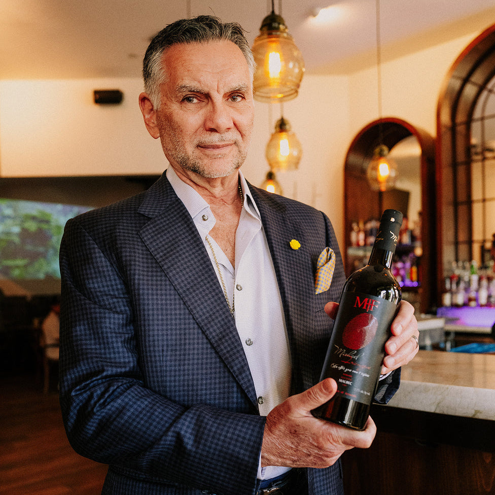 Man in a suit holding a bottle of wine in a bar setting