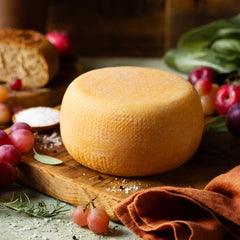 Round cheese on a wooden board with grapes and bread in the background