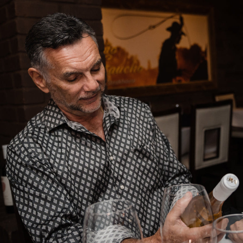 Man sitting at a table in a dimly lit restaurant, enjoying wine.