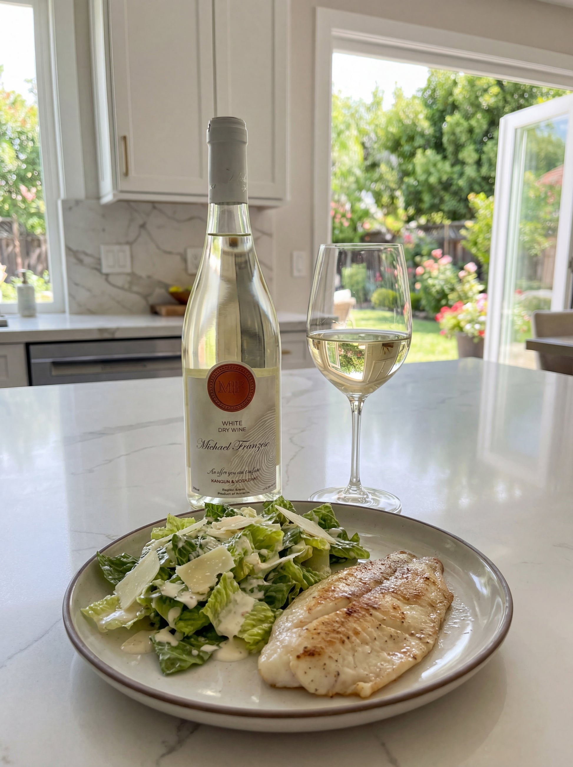 Bottle of white wine, glass of white wine, and plate with salad and fish on a kitchen counter.