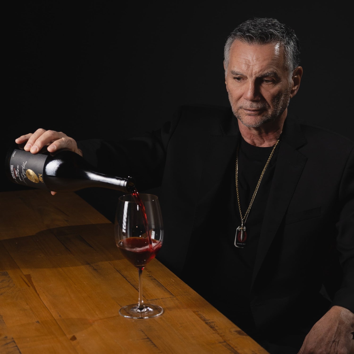Man pouring red wine into a glass on a wooden table with a dark background