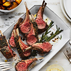 Grilled lamb chops on a white plate with rosemary and a side dish.