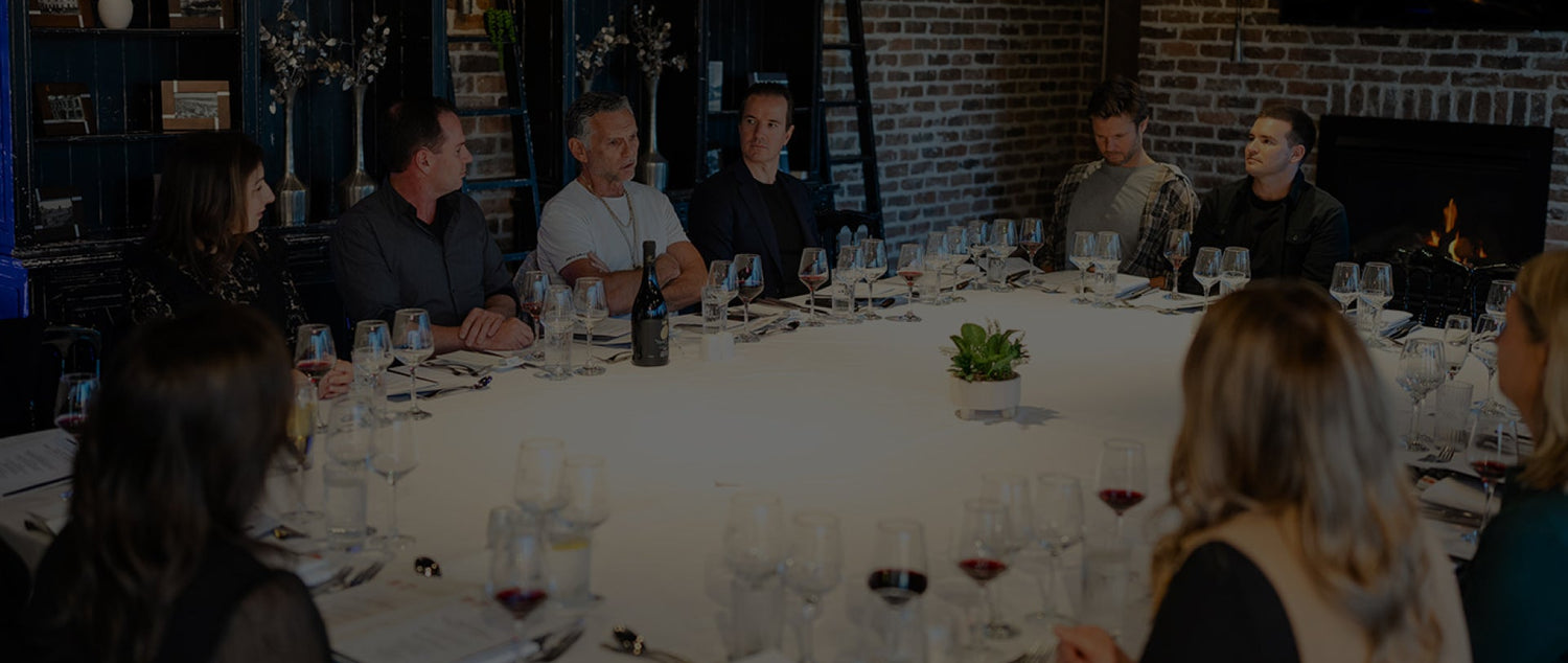 Group of people sitting around a dining table with wine glasses and bottles in a restaurant setting.