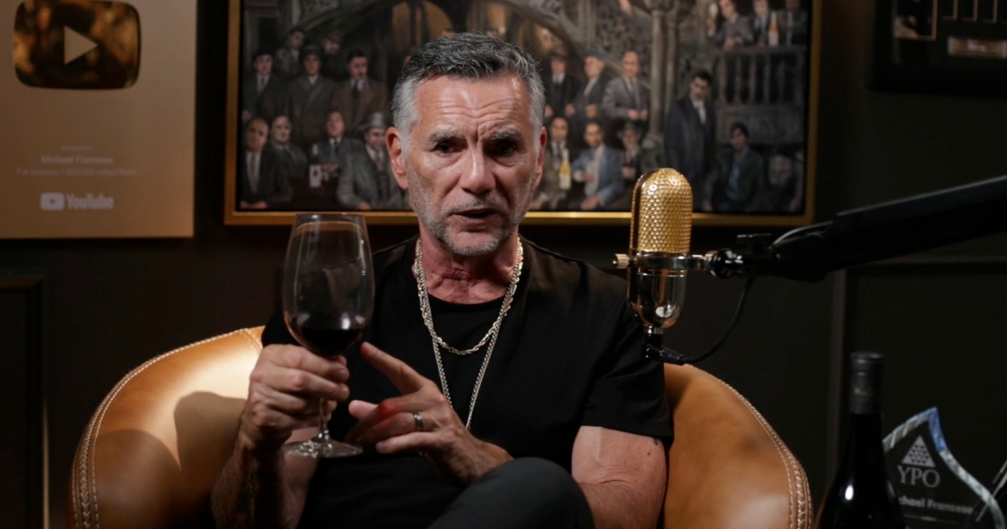 Man holding a glass of red wine in a studio setting with a microphone and awards.