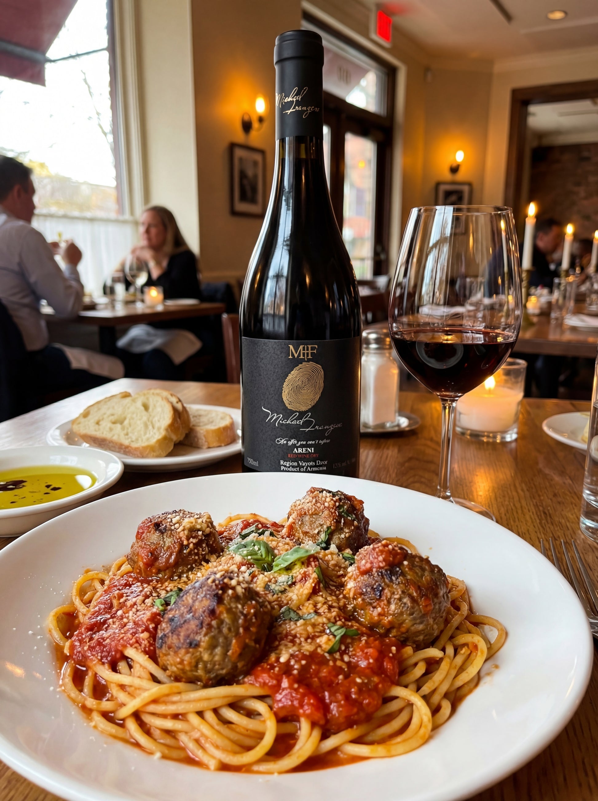 Spaghetti with meatballs on a plate with a bottle of wine and glasses in a restaurant setting.